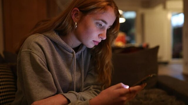 junge Frau schreibt abends mit ihrem Smartphone, das Gesicht wird dabei vom Display angeleuchtet