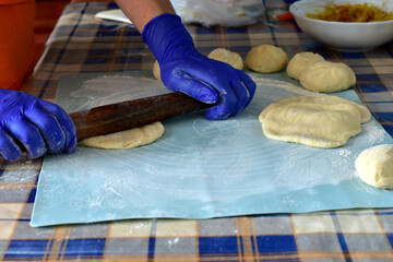 The chef rolls out a piece of dough on the table for baking buns.