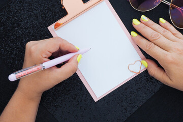 the left female hand writes on a clipboard with a pen. shiny black background..