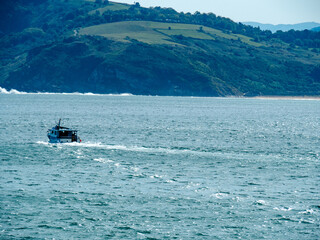 fishing boat sailing with hills in the background and sky with some clouds