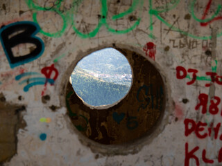 hole in concrete in an old construction that reveals a mountain and houses on the other side