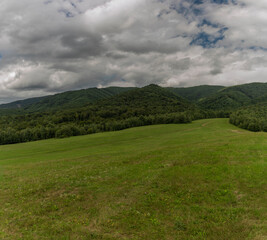 Fototapeta na wymiar Panorama view with meadows and pasture land and gray clouds near Runina village
