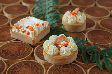 dessert, cheesecake with mango and passion fruit in the form of brownies with mousse on top. Decorated with cookies in the form of a heart. On a wooden table in a white plate
