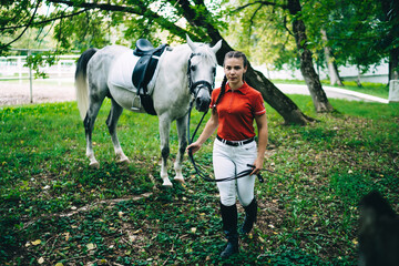 Portrait of attractive Caucasian brunette woman posing near mare horse, beautiful female jockey enjoy spending time on farm for training and practicing horseback riding with stallion animal