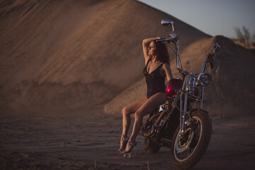 Beautiful sexy woman in lace bodysuit and high heels sits on a motorcycle on an industrial background