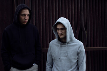 Two guys in hoodies against a background of rusty pipes. Two guys in a light and dark hoodie with a hood on their head.