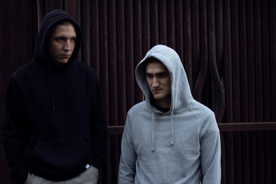 Two guys in hoodies against a background of rusty pipes. Two guys in a light and dark hoodie with a hood on their head.