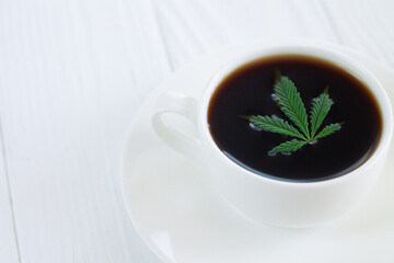White cup of cannabis coffee with hemp leaves close-up