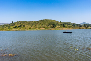 Awesome view of small lake  with a fishing boat near a greenery mountain background.
