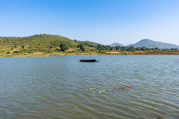 Awesome view of small lake  with a fishing boat near a greenery mountain background.
