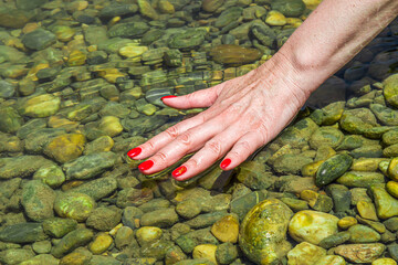 Female hand with a beautiful manicure in river water.