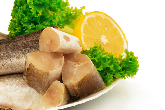 Raw slices of fish hake, pollock on the plate with lemon and leaves of salad lettuce on white background.