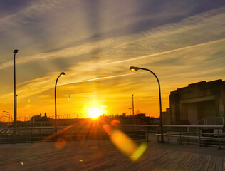 Orange Sunset Over Boardwalk, with Orange Sun just over Buildings. High quality photo. Lamp Poles...