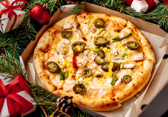 Mexican pizza for Christmas with chicken fillet, mozzarella cheese, jalapeno peppers, tomatoes, onions, corn, bell pepper with Christmas decorations, gifts, spruce, toys