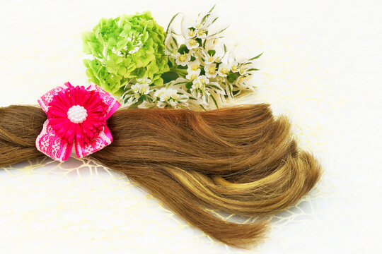 Hair and barrette with pink ribbon, flowers and green leaf on white lace background.