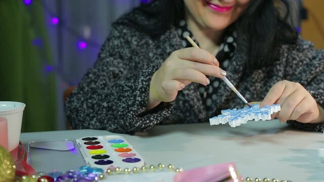 Woman's hands make home decorations for Christmas by painting white blanks with watercolors