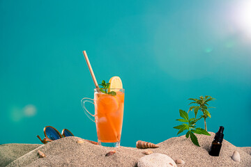 Lemonade in different glasses / jars, CBD dropper oil and a twig of marijuana plant in the sand. Sunglasses and seashells can be seen from the side. 