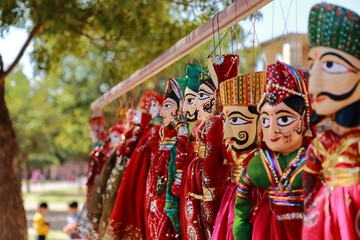 Colorful human face shaped Puppets wearing colorful clothes hanging against the wall in Rajasthan...