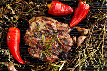 Grilled pork neck with aromatic herbs, garlic and chili peppers on a cast iron grill, top view