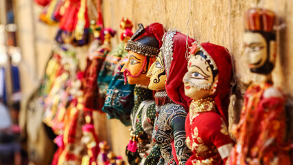 Colorful human face shaped Puppets wearing colorful clothes hanging against the wall in Rajasthan...