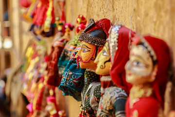 Colorful human face shaped Puppets wearing colorful clothes hanging against the wall in Rajasthan...