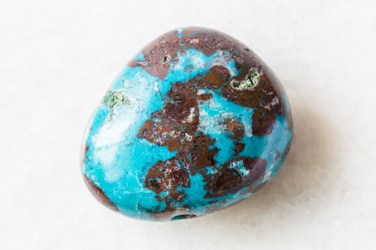 closeup of sample of natural mineral from geological collection - tumbled Chrysocolla with Cuprite rock on white marble background