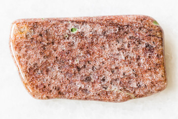 closeup of sample of natural mineral from geological collection - polished red Aventurine rock on white marble background from Taganay, South Ural, Russia