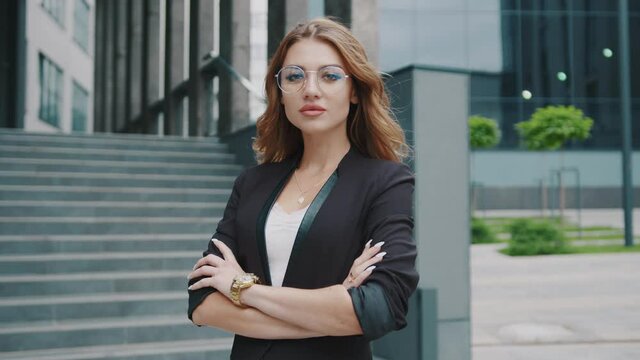 Attractive young businesswoman with glasses standing look at camera near business center outdoor. Corporate building. Fashion outside office. Leader success confidence. Happy portrait slow motion.