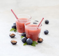 Nectar fruit of black plums in a glass with bamboo straws on a light gray background