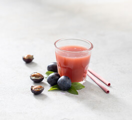 Nectar fruit of black plums in a glass with bamboo straws on a light gray background