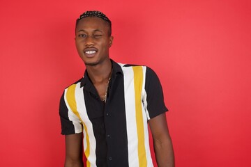 African american man with braids wearing casual shirt over isolated red background winking looking...