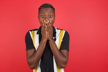 Vivacious African american man with braids wearing casual shirt over isolated red backgro , giggles joyfully, covers mouth, has fun alone,  has natural laughter, hears positive story or funny anecdote