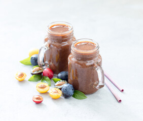 Fruit smoothie of red, yellow and black plums in a glass jar with bamboo straws on a light gray background