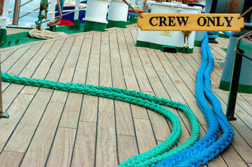 Deck of a boat with several ropes and a sign where it puts only the crew