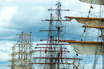 The masts of several ships, with flags and sails and in the background a beautiful sky with clouds