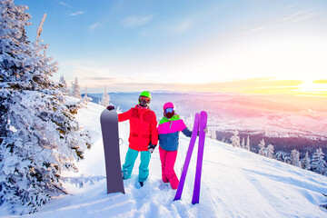 Loving couple snowboarder and skier hold hands on a background of mountains in the winter forest,...
