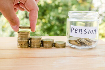 A woman's hand puts a coin on a stack with coins, a glass jar full of coins. Pension fund concept.