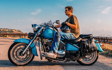Fototapeta na wymiar Biker on a turquoise motorcycle on the edge of the road