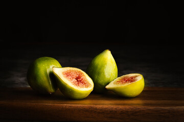 Baroque style still life. Three figs, two whole and one cut in half on wooden board and dark...