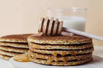 Close up of a honey dipper pouring honey over a pile of waffles