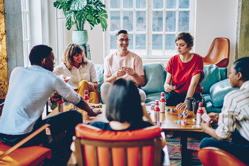 Happy multicultural hipster guys playing in gambling sitting at table with poker chips and cards,...