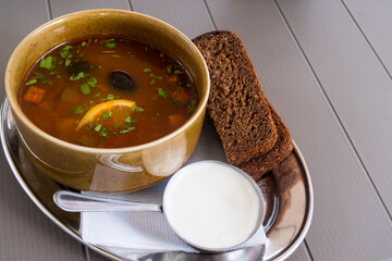 Traditional Russian meat soup solyanka in a bowl, with sour cream and black bread. Krasnaya Polyana, Sochi, Russia