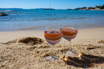 Two glasses of local rose wine on white sandy beach and blue Mediterranean sea on background, near Le Lavandou, Provence, France