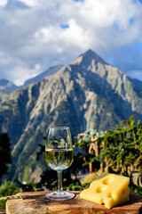 Glass of swiss or savoy dry white wine and yellow emmental cheese with Alpine mountains peaks on background