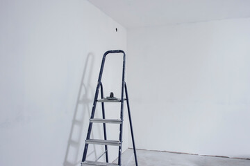 A blue stepladder stands in an all-white room