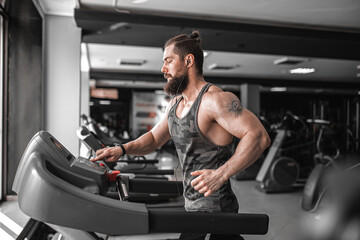 Fototapeta na wymiar Adult strong bearded man running on treadmill in gym.