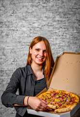 portrait of young teenager brunette girl with long hair with box of pizza on gray wall background