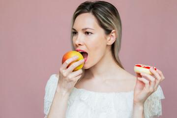 beautiful girl makes a choice between an apple and a cake, diet and proper nutrition, on a pink background