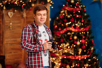 male photographer in a plaid shirt with a camera at the Christmas tree. traditional New year family photo sessions in the Studio. seasonal work. festive atmosphere.