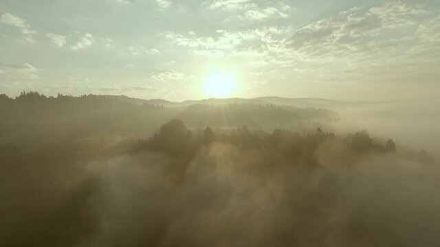 Fog around hills during a cinematic sunrise with rays of light and blue sky